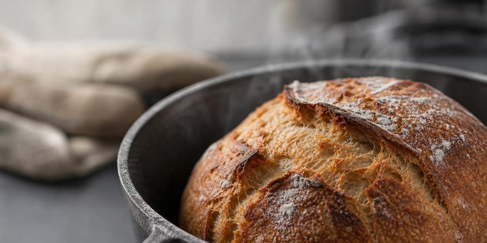 Frisch gebackener Brotlaib mit aufgerissener Kruste dampft im gusseisernen Topf.