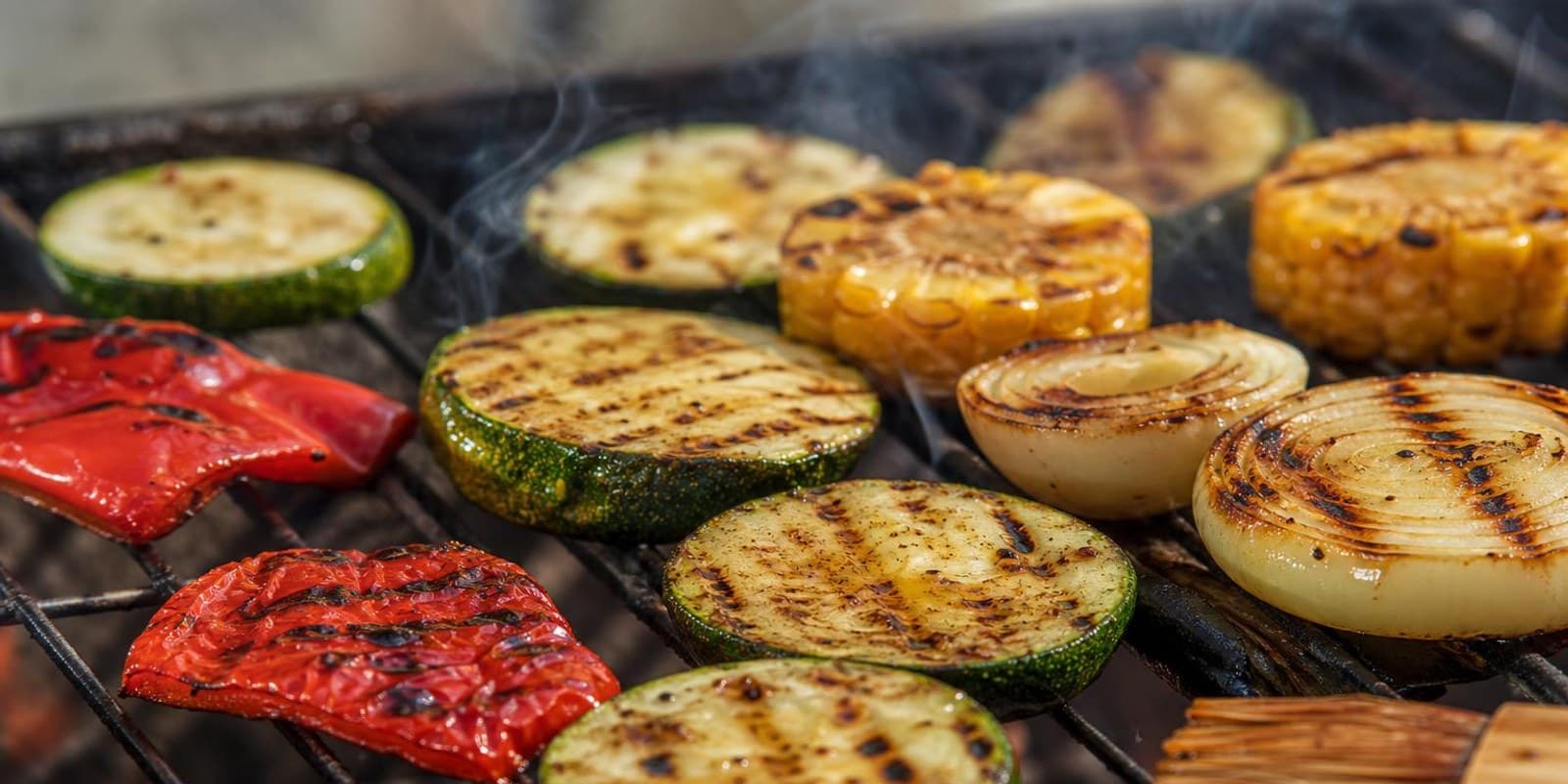 Buntes Gemuese mit Roestspuren brutzelt dicht an dicht auf dem Grillrost.