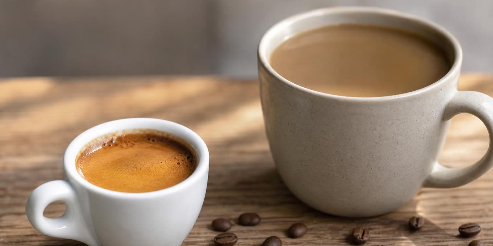 Kleine Espressotasse mit Crema neben einer grossen Tasse Filterkaffee auf einer Holzplatte.