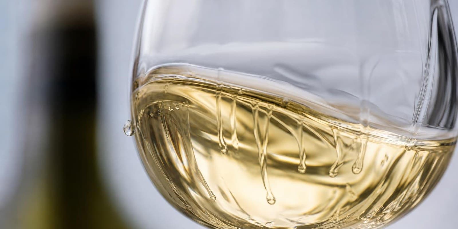 Hellgoldener Weisswein schwenkt im Glas, an der Innenwand laufen langsame Schlieren herab.