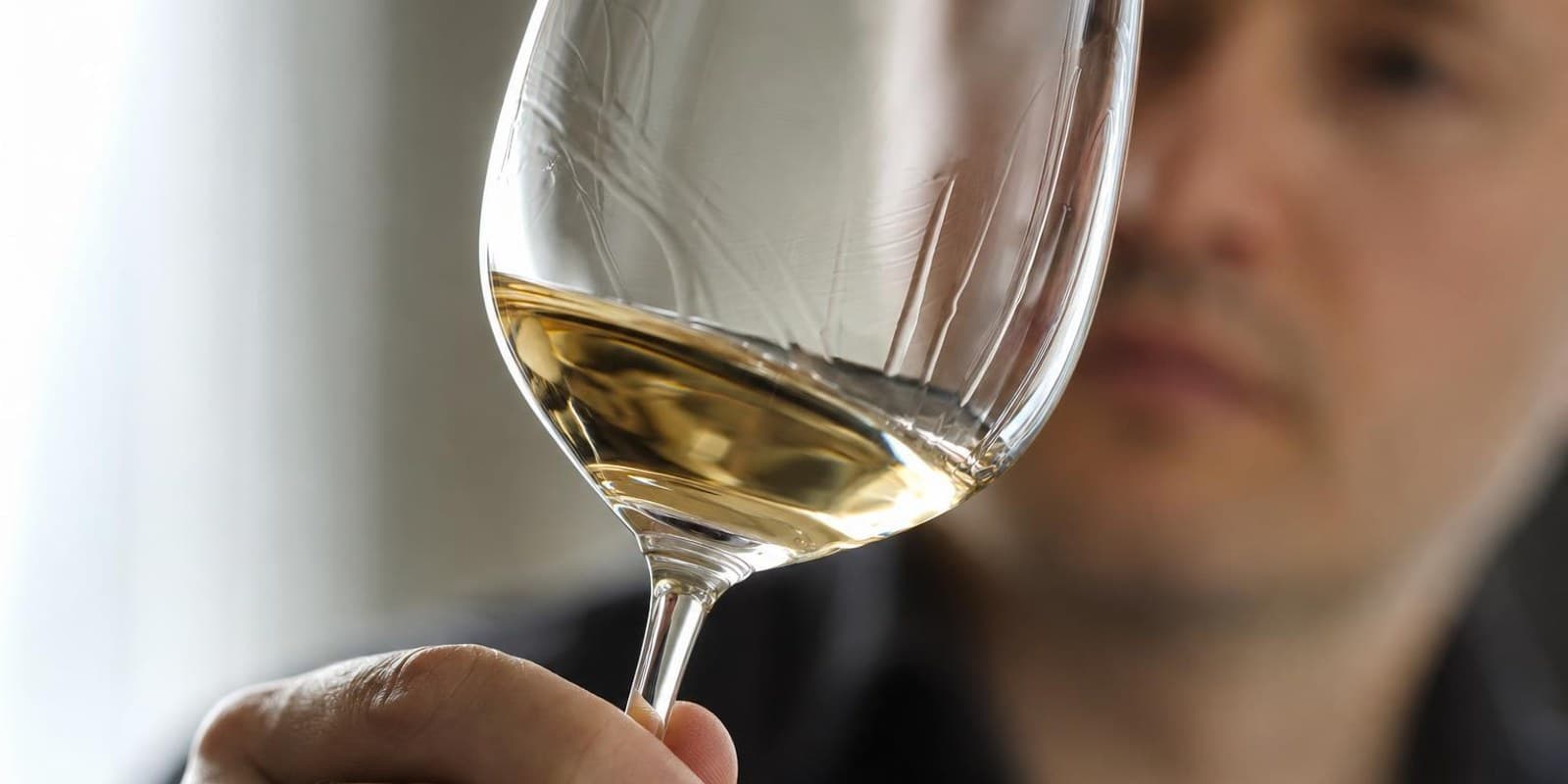 Eine Hand schwenkt Weisswein im Glas, an der Innenseite laufen feine Schlieren herab.