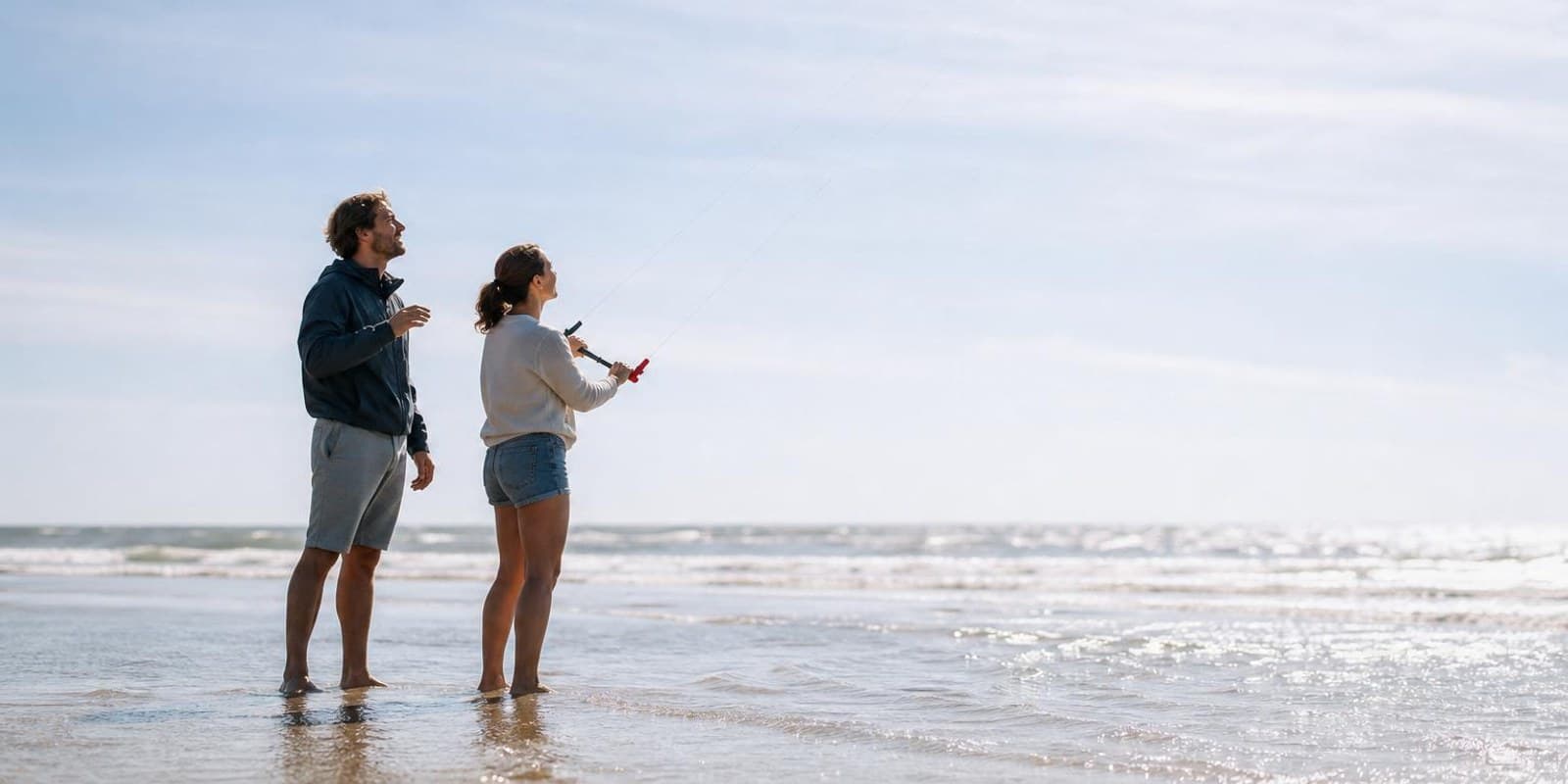 Kite-Anfaenger uebt mit Trainerkite am Strand, der Lehrer steht direkt dahinter.