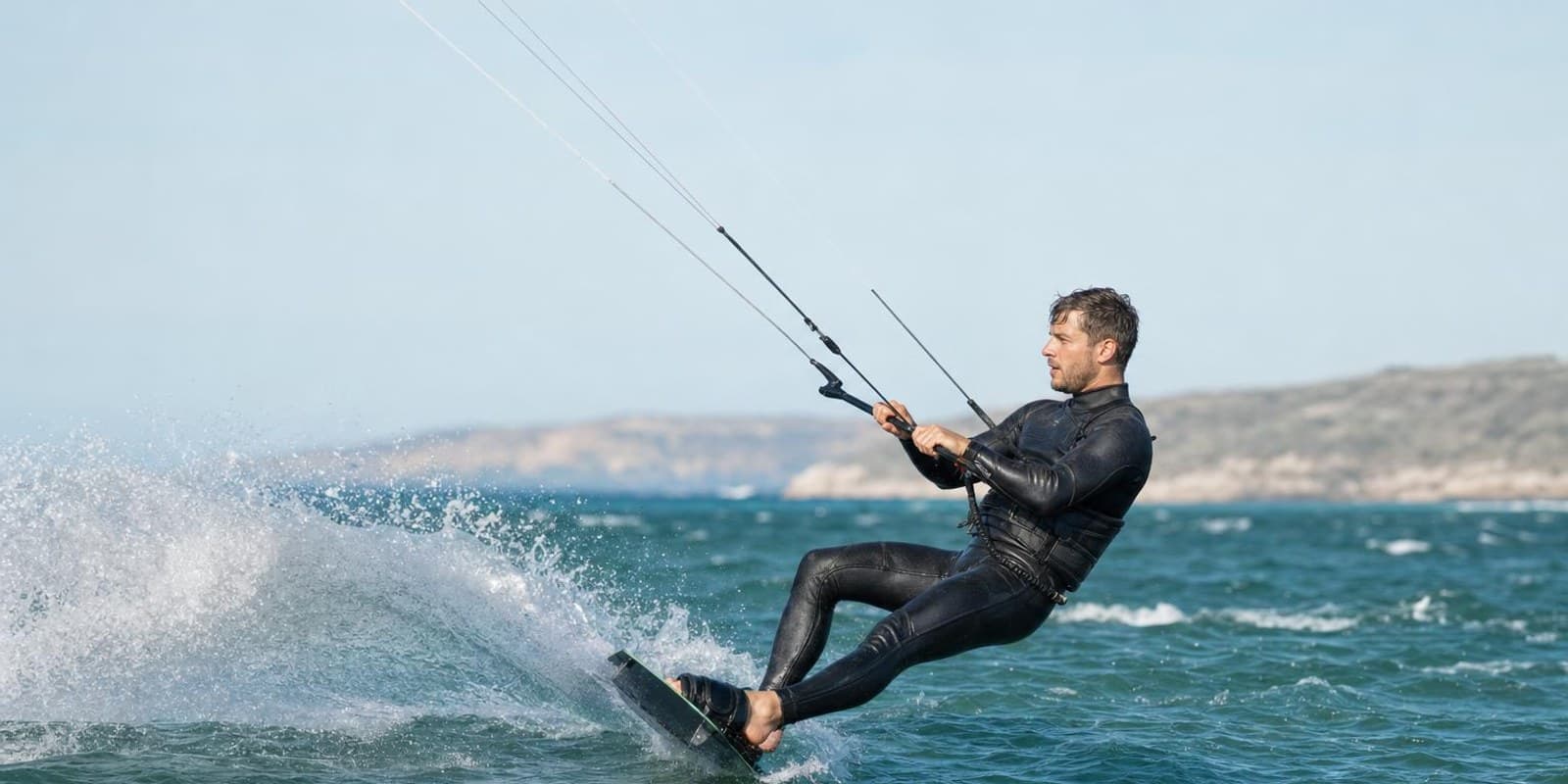 Ein Kitesurfer richtet sich beim Wasserstart aus dem Wasser auf, waehrend der Kite ihn nach vorn zieht.