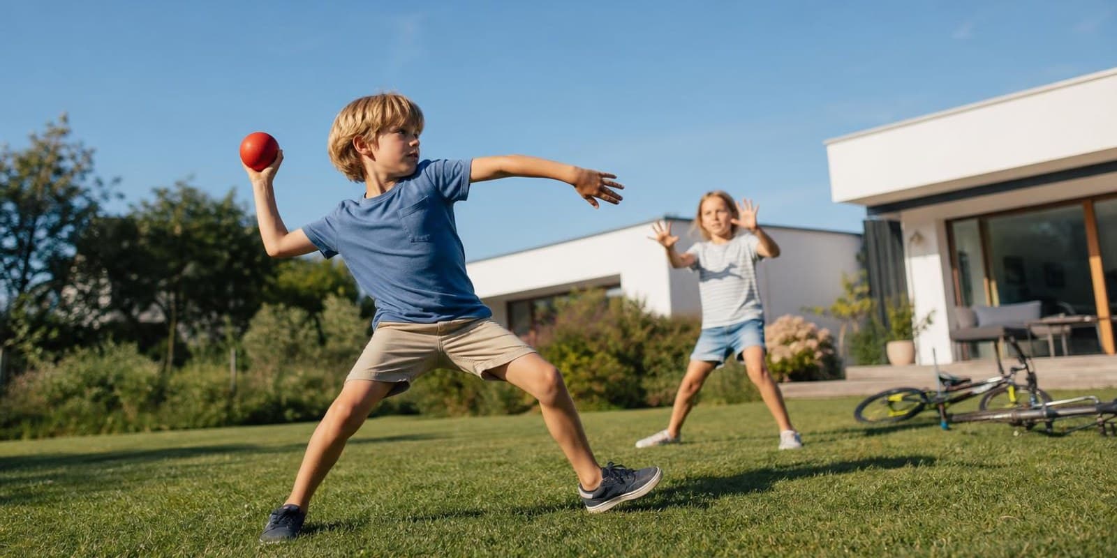 Kinder spielen bei hellem Tageslicht draussen im Garten und schauen dabei in die Ferne.