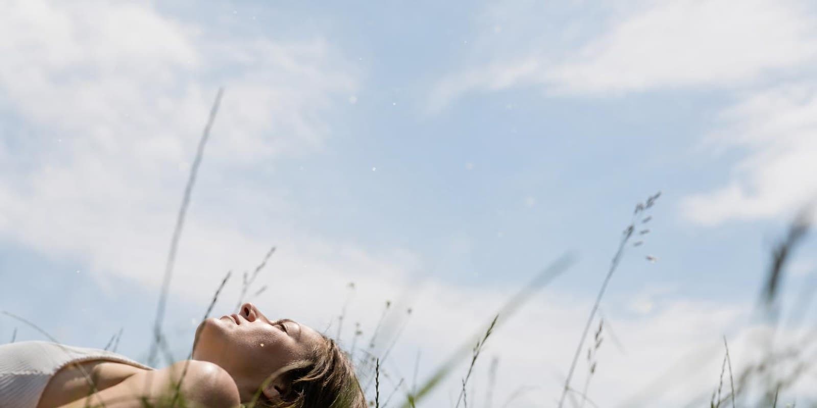 Person liegt in einer Wiese und blickt in den hellen Sommerhimmel.