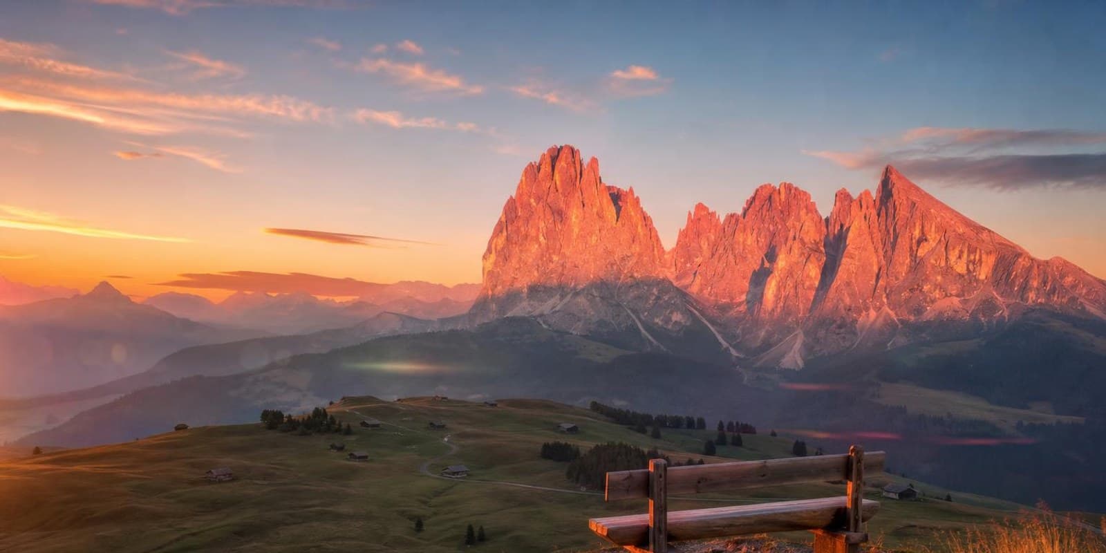 Dolomitengipfel gluehen bei Sonnenuntergang rosa ueber gruenen Almwiesen.