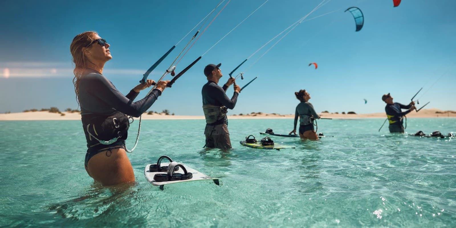 Kite-Anfaenger ueben huefttief im flachen tuerkisen Wasser einer sonnigen Lagune.