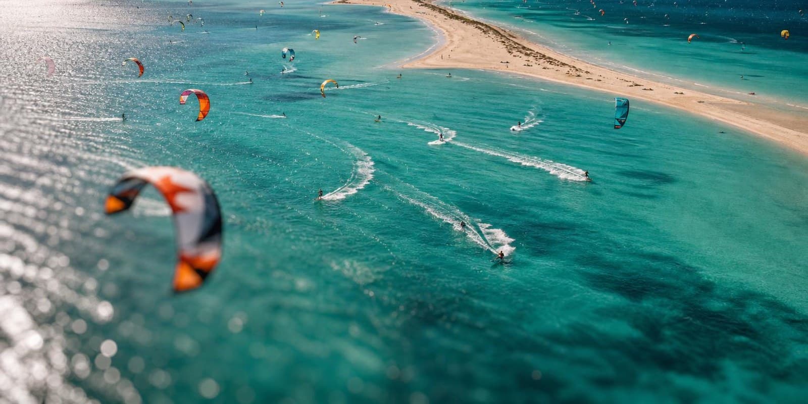 Luftaufnahme einer tuerkisen Lagune voller bunter Kites in der Hochsaison.