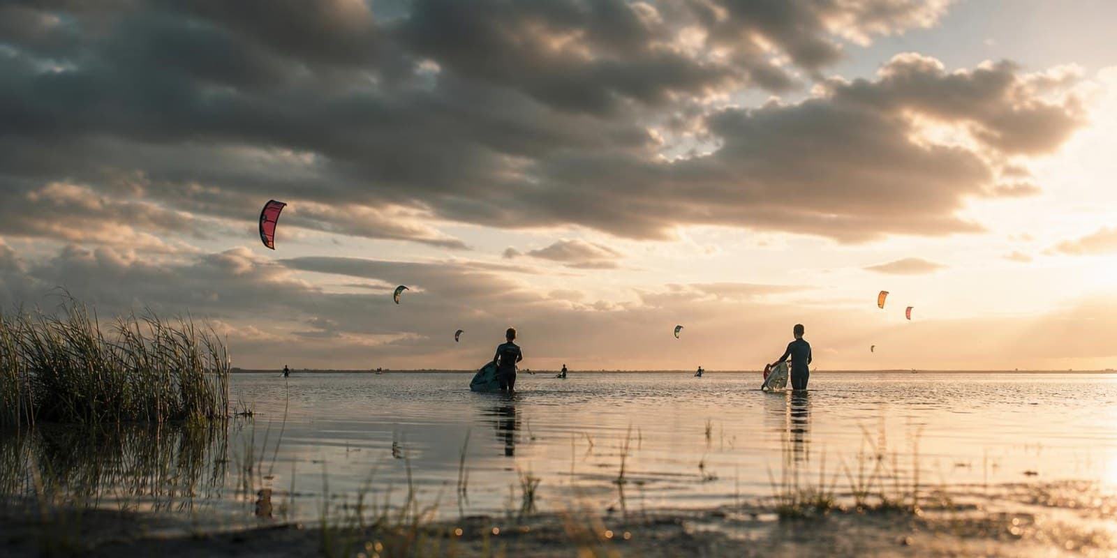 Kitesurfer stehen weit draussen im flachen Wasser des IJsselmeers unter weitem Himmel.