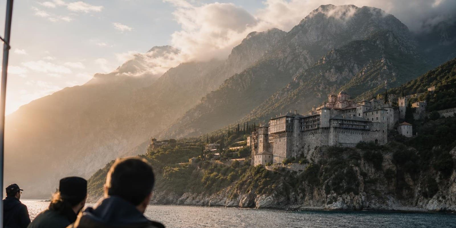 Ausflugsboot passiert ein maechtiges Kloster am steilen Haenge des Berges Athos ueber dem Meer.