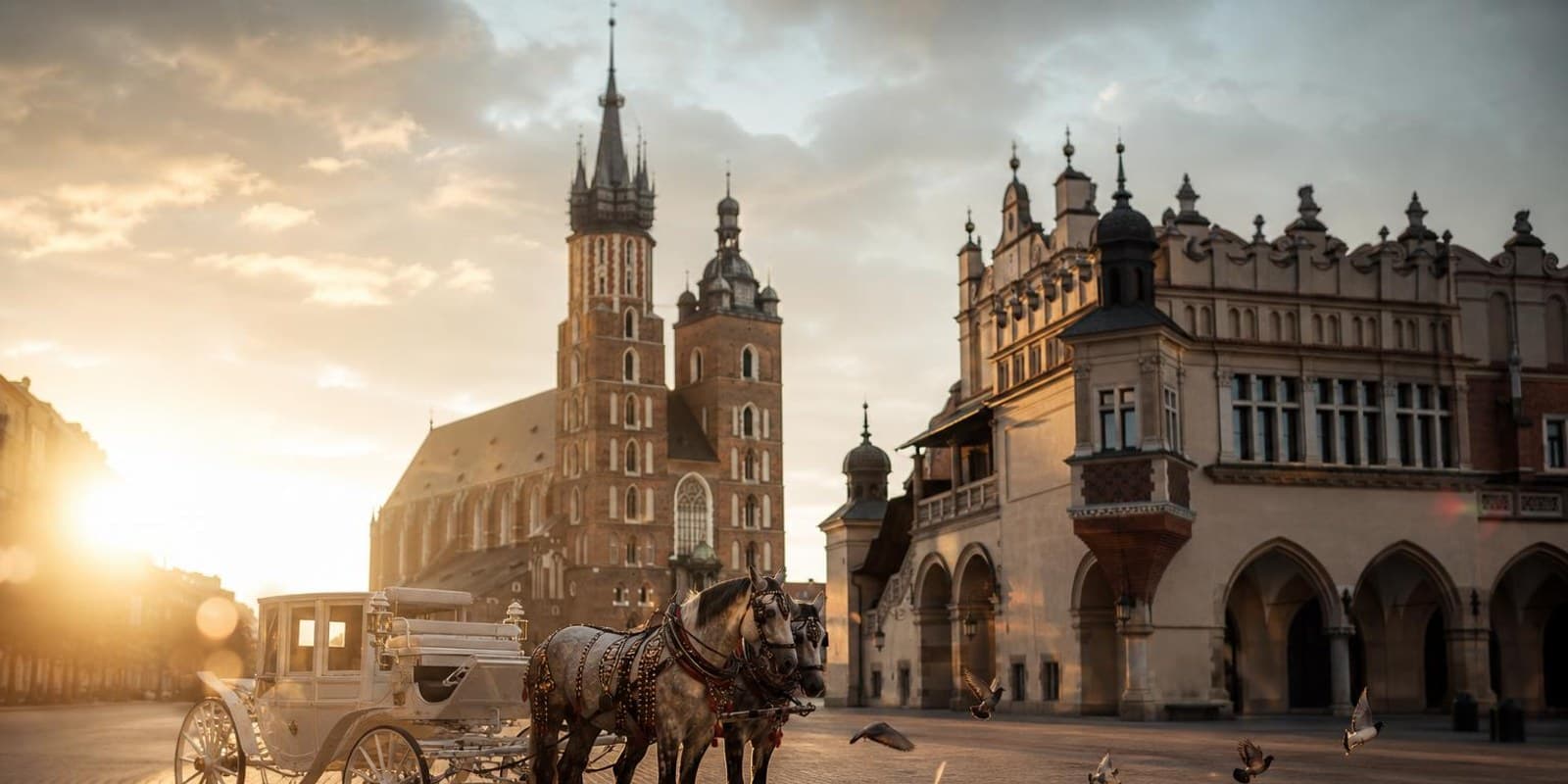 Der grosse Hauptmarkt von Krakau mit Tuchhallen und Marienkirche im fruehen Morgenlicht.