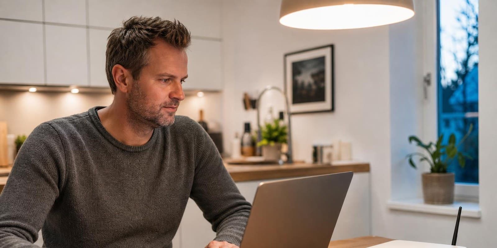 Mann sitzt mit Laptop neben dem Router und kuemmert sich um die Einstellungen.