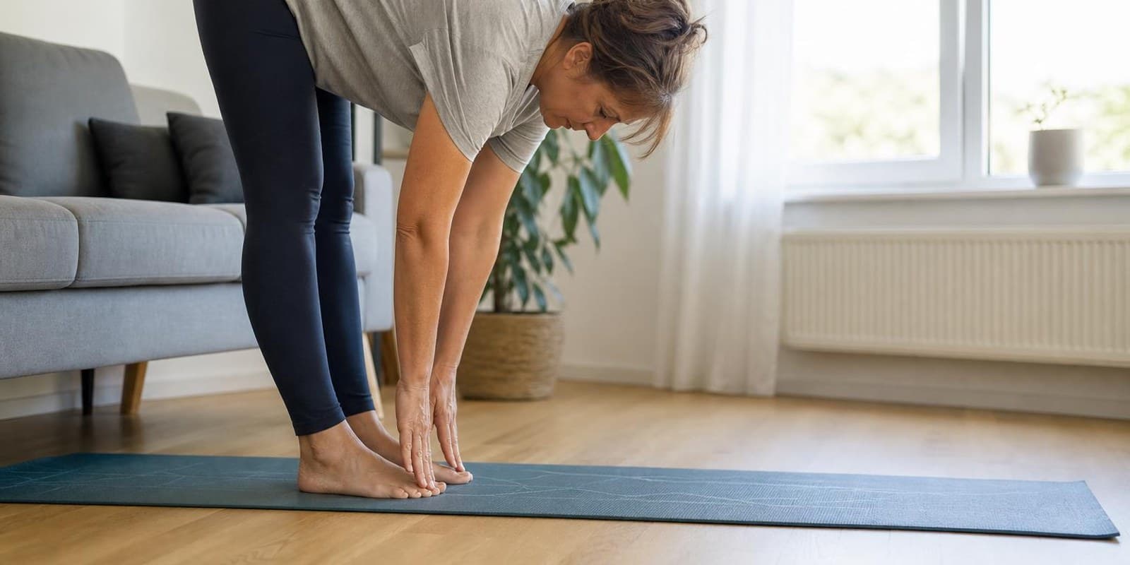 Frau testet auf einer Matte im Wohnzimmer mit dem Zehenspitzen-Test ihre Beweglichkeit.