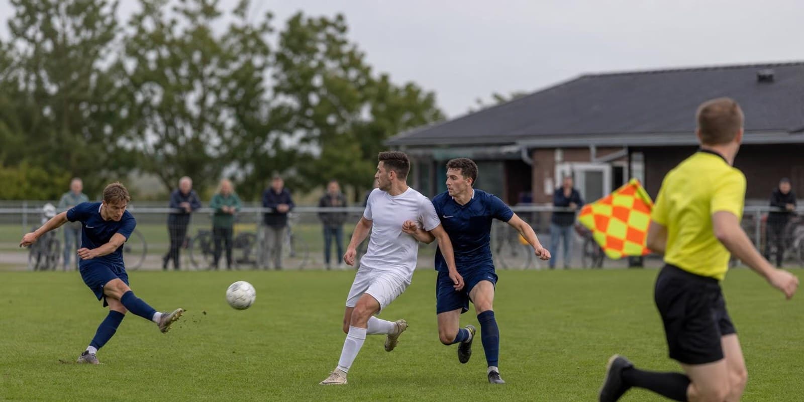 Stuermer und letzter Verteidiger sprinten beim Abspiel auf gleicher Hoehe, der Linienrichter beobachtet.