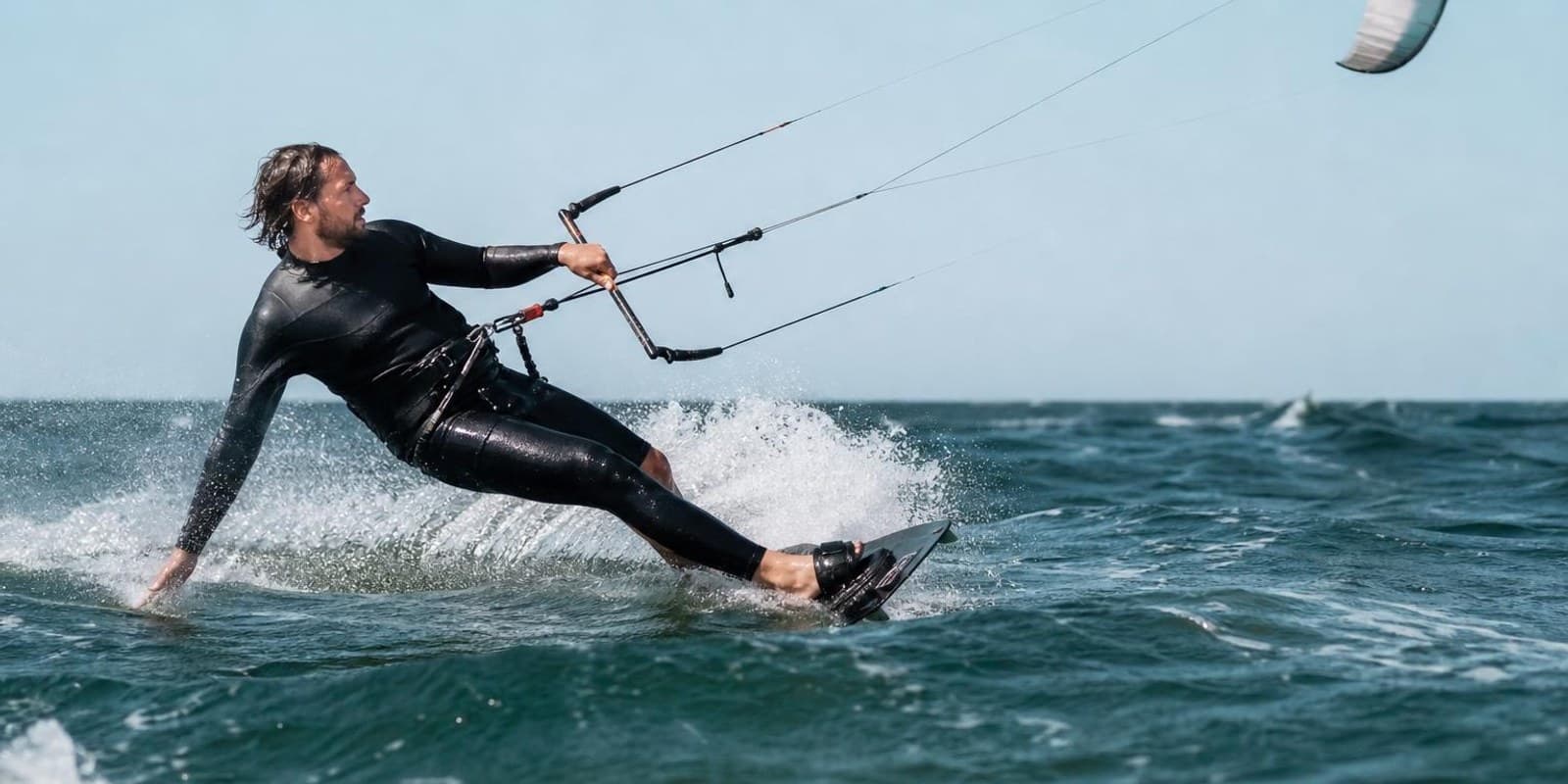 Kitesurfer kantet sein Board hart gegen den Wind und zieht eine weisse Spur durchs Wasser.