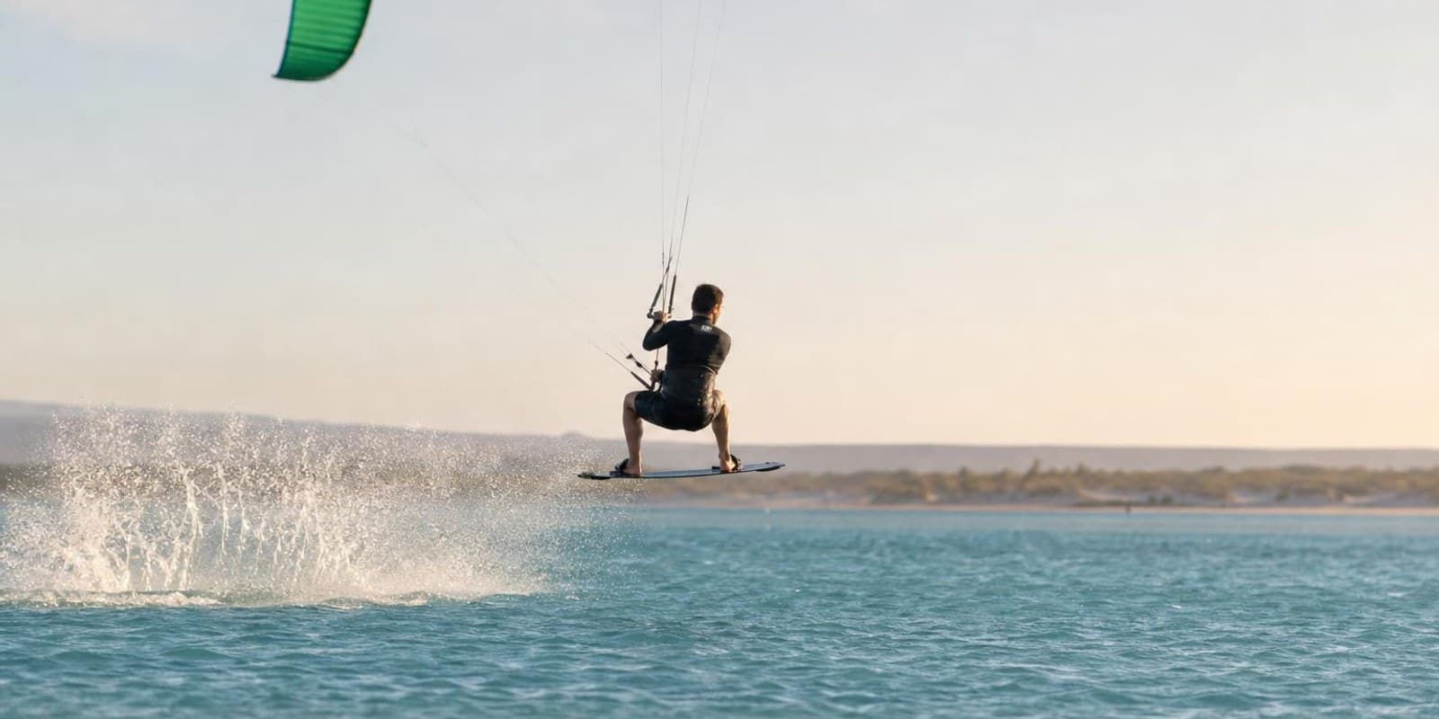 Kiter schwebt bei seinem ersten kontrollierten Sprung knapp ueber dem flachen Wasser.