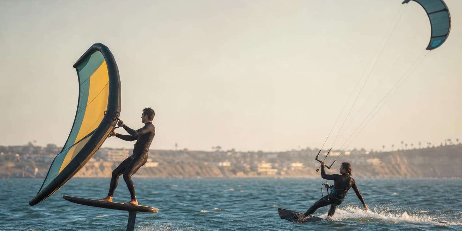 Wingfoiler und Kitesurfer fahren auf demselben Revier nebeneinander uebers Wasser.