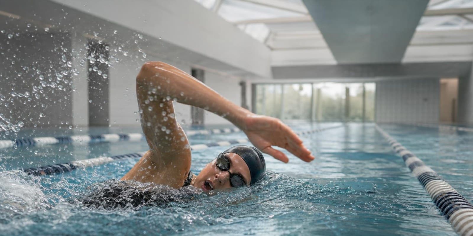Kraulschwimmerin zieht kraftvoll durch ihre Bahn im Hallenbad, das Wasser schaeumt.