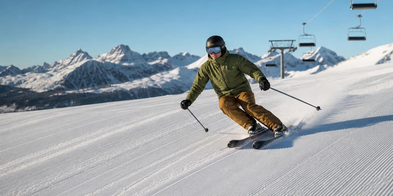 Skifahrer mit Helm zieht entspannte Schwuenge auf einer sonnigen, breiten Piste.