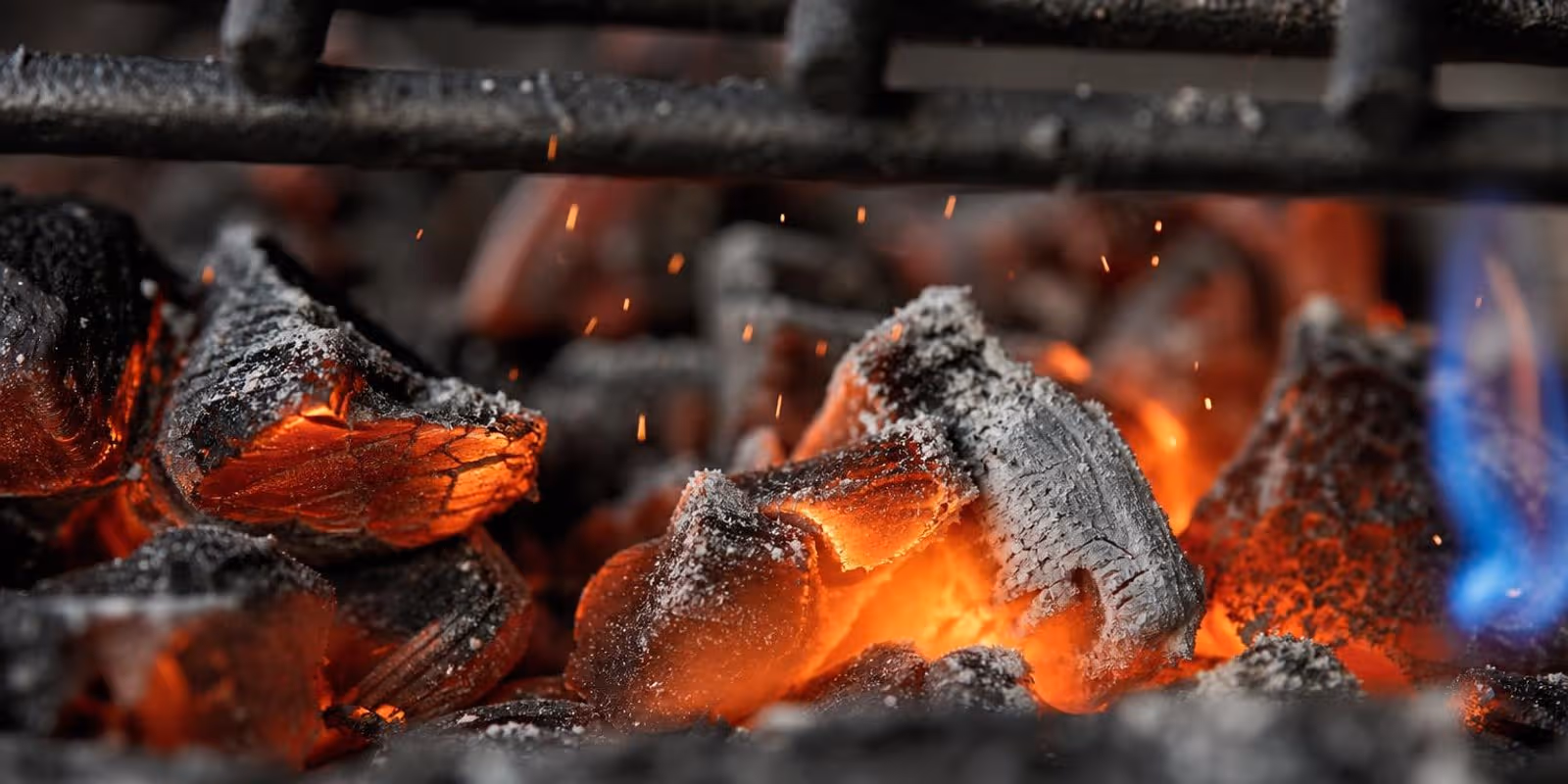 Gluehende Holzkohle unter dem Grillrost mit aufsteigenden Funken in Nahaufnahme.
