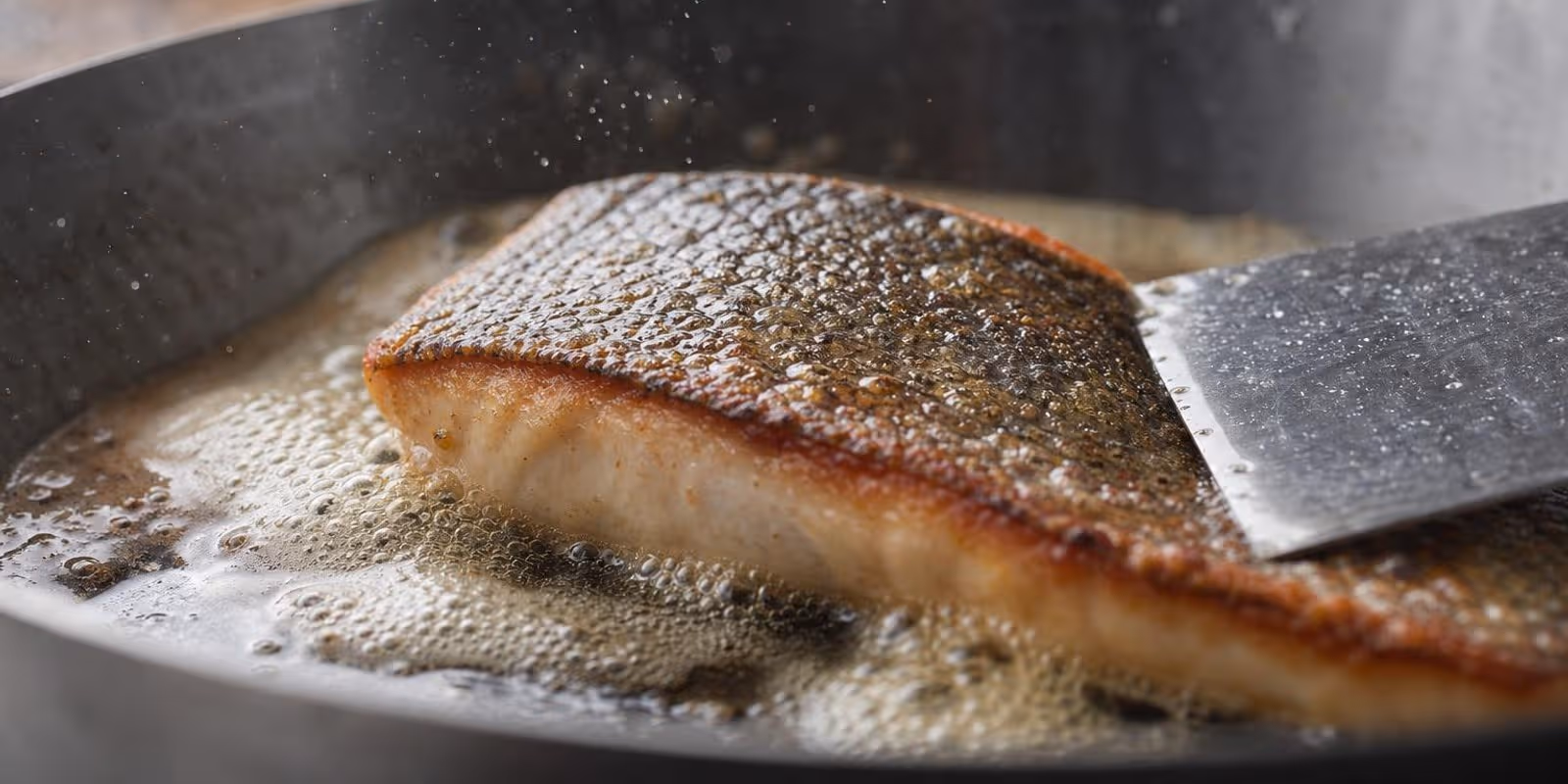 Fischfilet braet mit knuspriger Hautseite in einer heissen Pfanne.