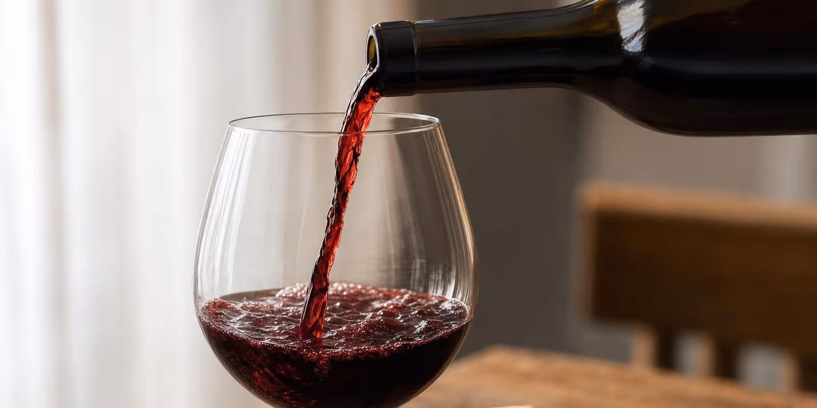 Rotwein wird in ein bauchiges Glas eingeschenkt, Licht scheint durch den fallenden Weinstrahl.