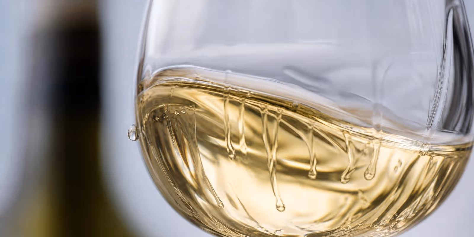 Hellgoldener Weisswein schwenkt im Glas, an der Innenwand laufen langsame Schlieren herab.