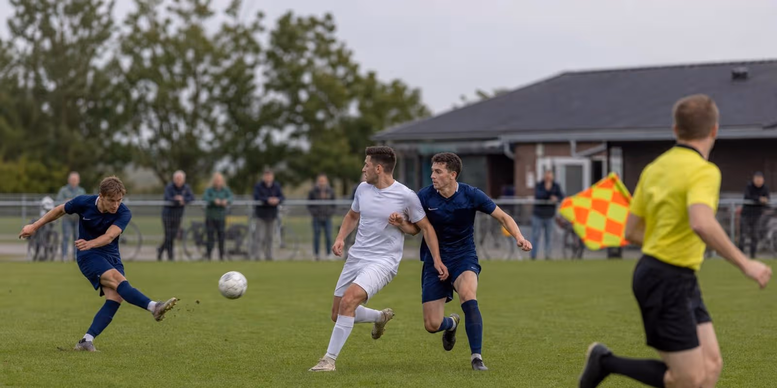 Stuermer und letzter Verteidiger sprinten beim Abspiel auf gleicher Hoehe, der Linienrichter beobachtet.