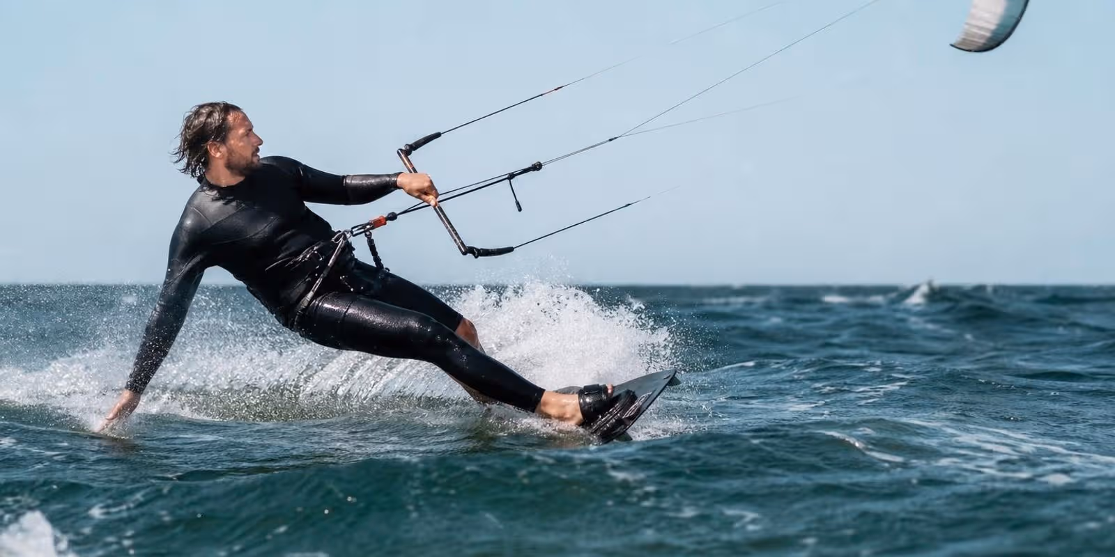 Kitesurfer kantet sein Board hart gegen den Wind und zieht eine weisse Spur durchs Wasser.
