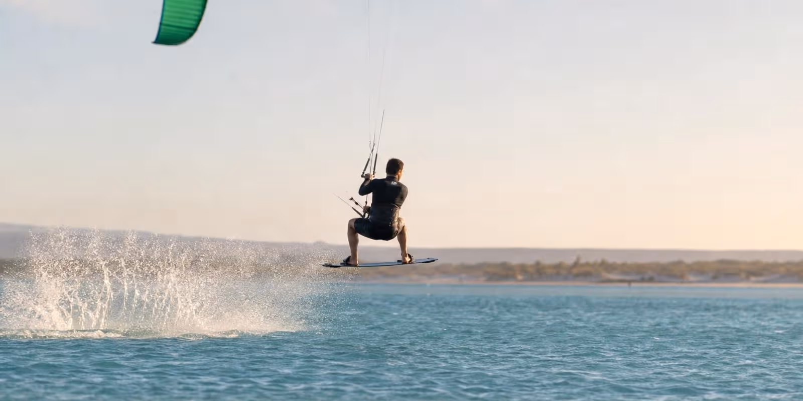 Kiter schwebt bei seinem ersten kontrollierten Sprung knapp ueber dem flachen Wasser.