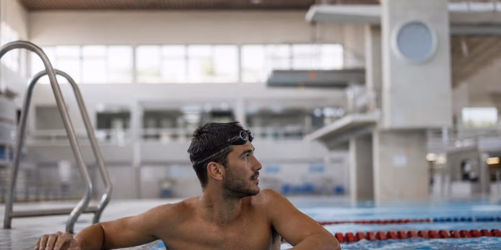 Schwimmer haengt zwischen zwei Serien am Beckenrand und blickt zur Tempouhr.
