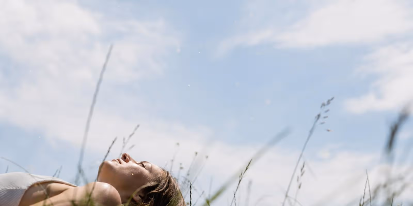 Person liegt in einer Wiese und blickt in den hellen Sommerhimmel.