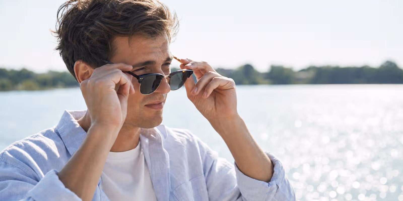 Ein Mann setzt an einem glitzernden See bei starkem Sonnenlicht eine Sonnenbrille auf.