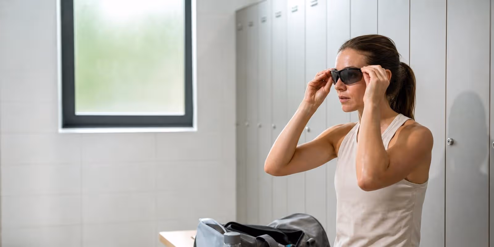 Sportlerin setzt in der Umkleide eine Sportbrille auf, im Rucksack liegt ein Kontaktlinsenbehaelter.