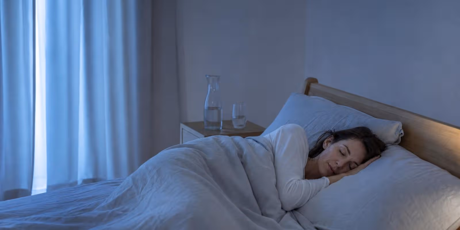 Person schlaeft tief und entspannt im blauen Licht der fruehen Morgenstunden.