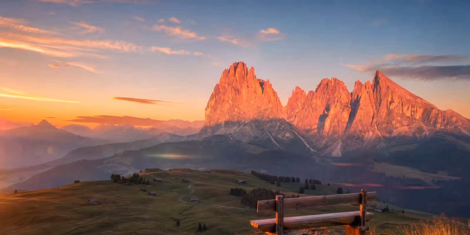 Dolomitengipfel gluehen bei Sonnenuntergang rosa ueber gruenen Almwiesen.