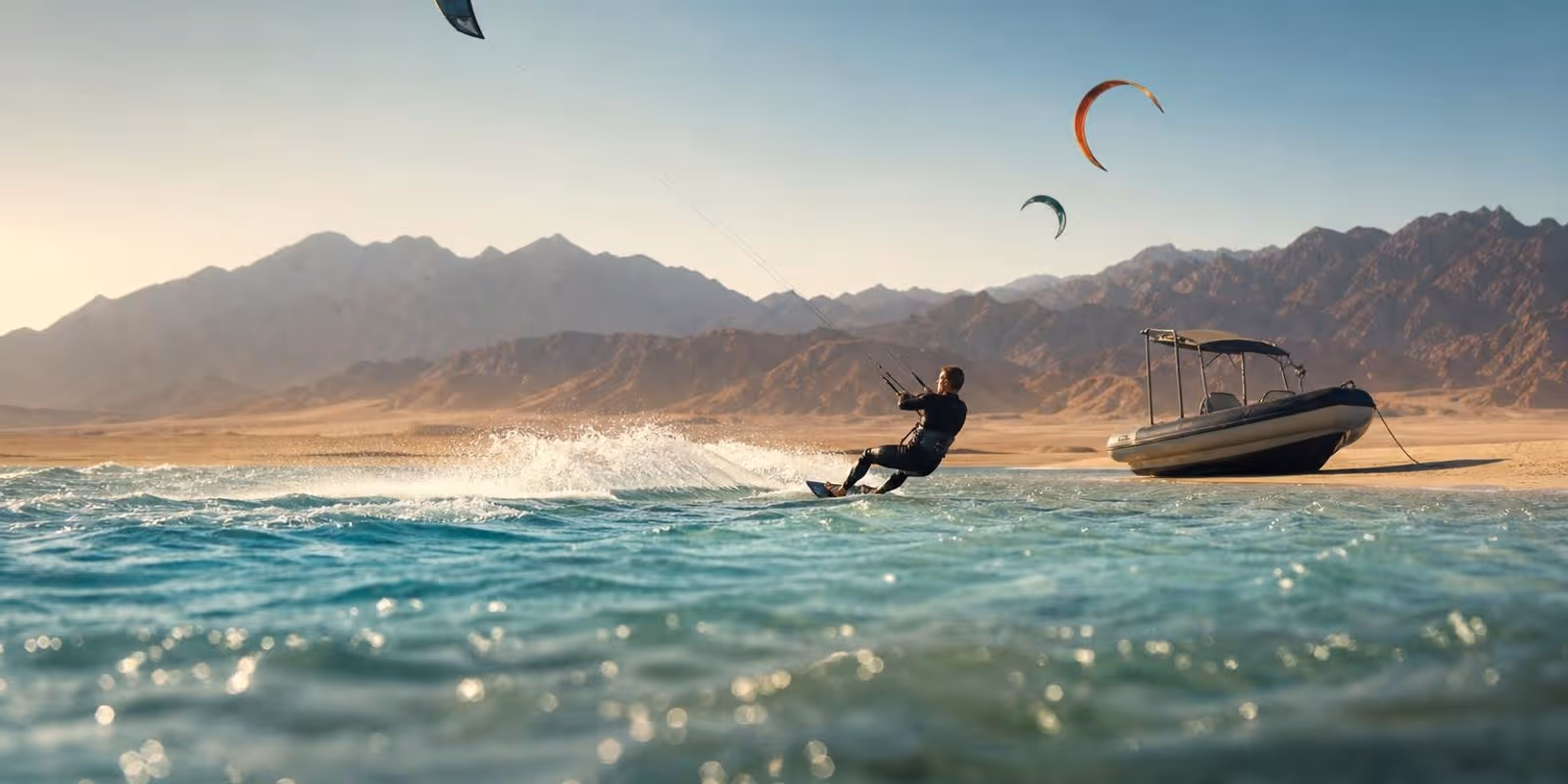 Safariboot ankert an einer Sandbank im Roten Meer, dahinter kreisen Kites vor Wuestenbergen.