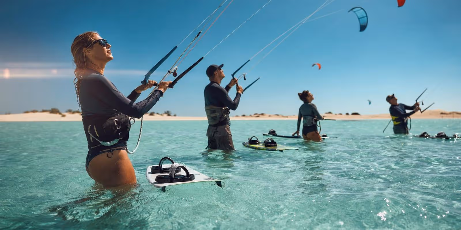 Kite-Anfaenger ueben huefttief im flachen tuerkisen Wasser einer sonnigen Lagune.