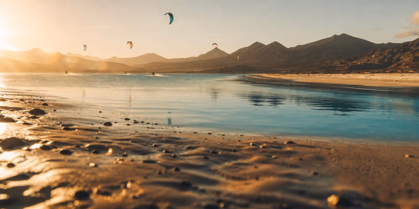 Riesige Gezeitenlagune mit Sandbank und Kites, dahinter karge Vulkanhuegel Fuerteventuras.