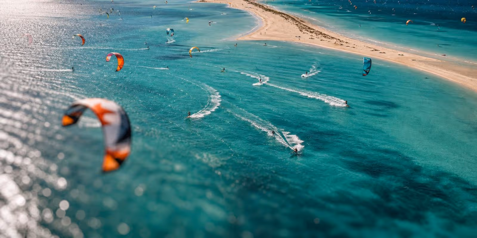 Luftaufnahme einer tuerkisen Lagune voller bunter Kites in der Hochsaison.