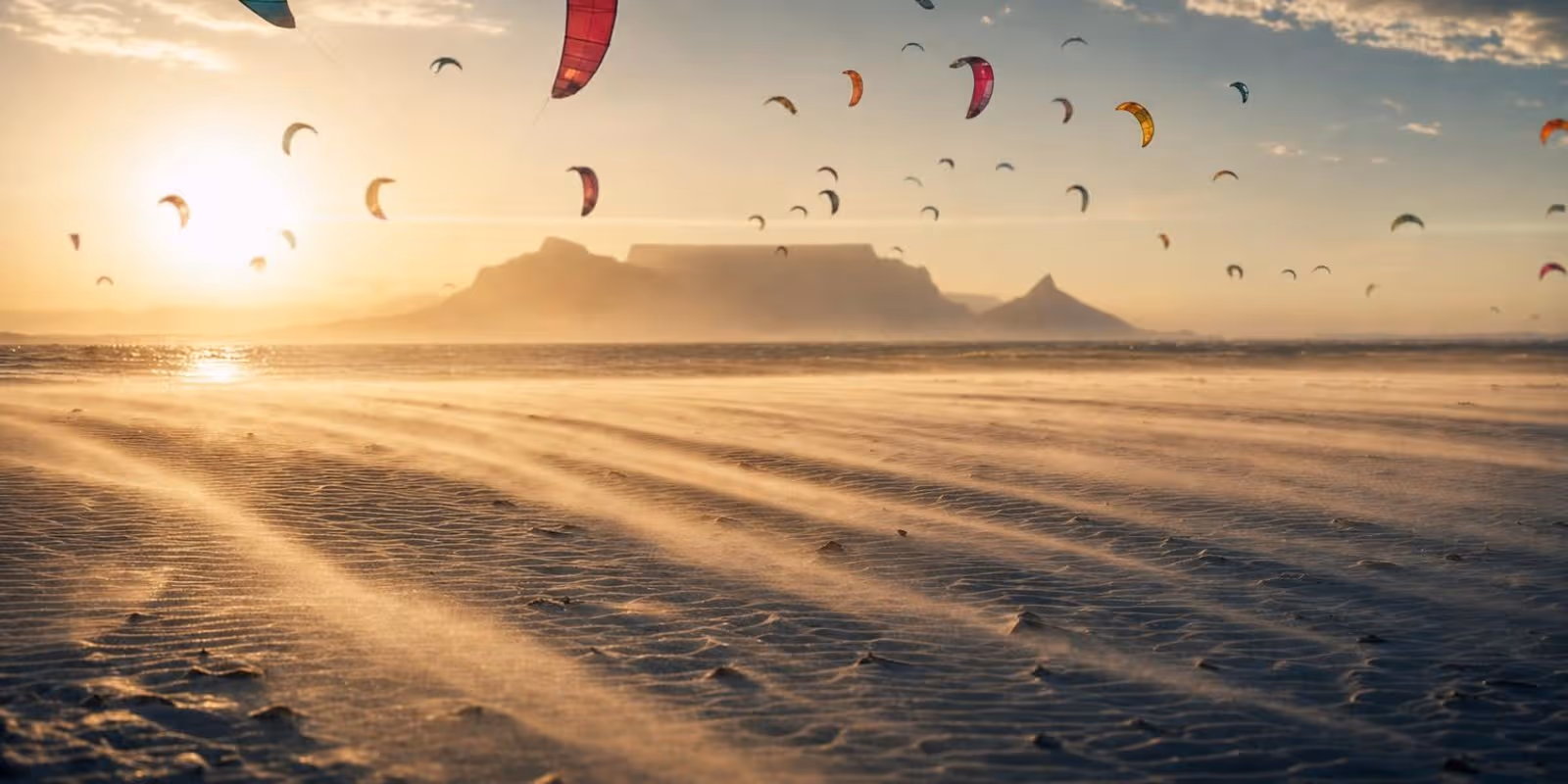 Zahllose Kites steigen ueber einem langen weissen Strand auf, waehrend Wind Sand ueber den Boden treibt.
