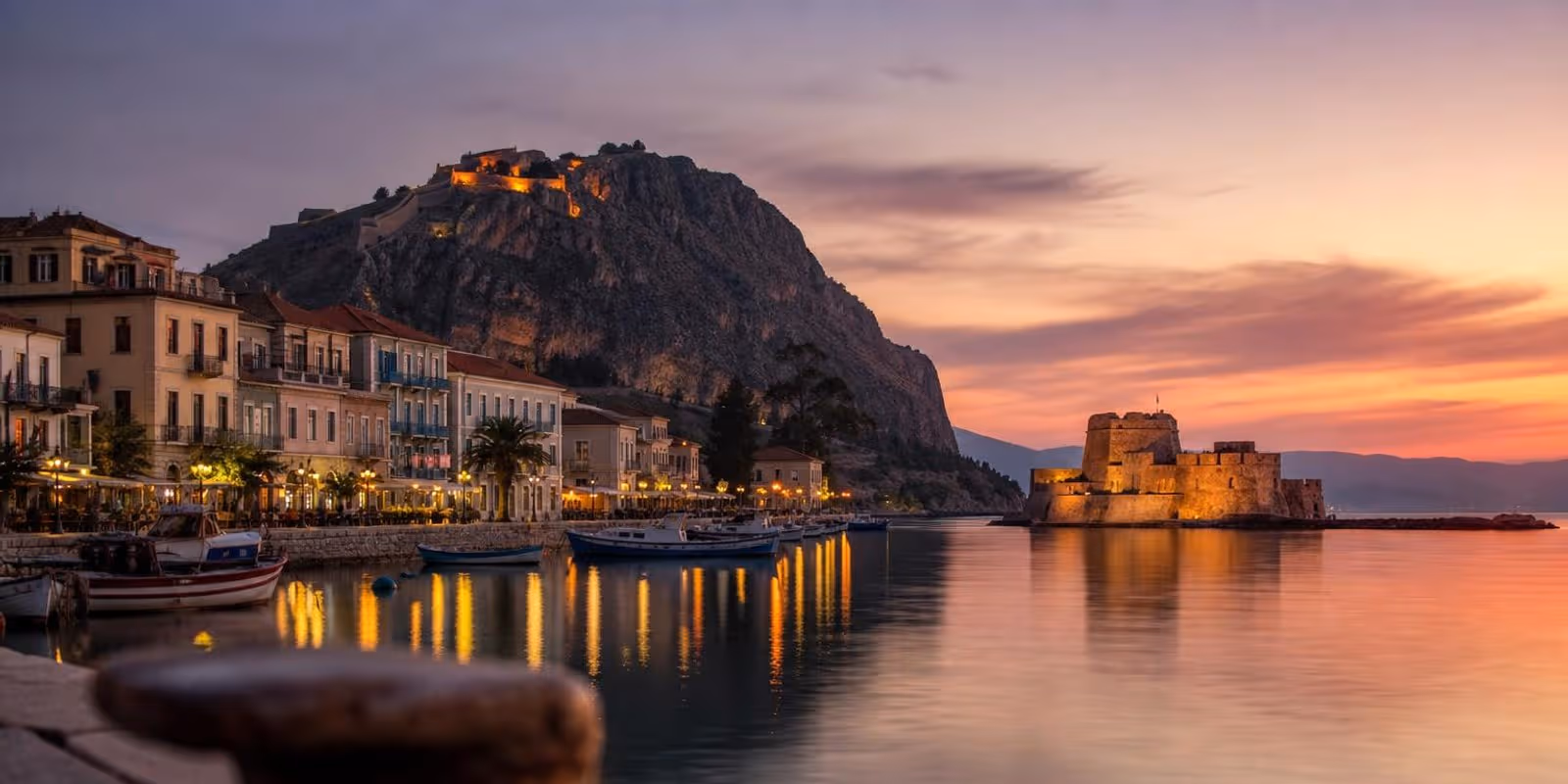 Abendstimmung im Hafen von Nafplio mit der kleinen Festungsinsel im Wasser und der Burg auf dem Felsen.
