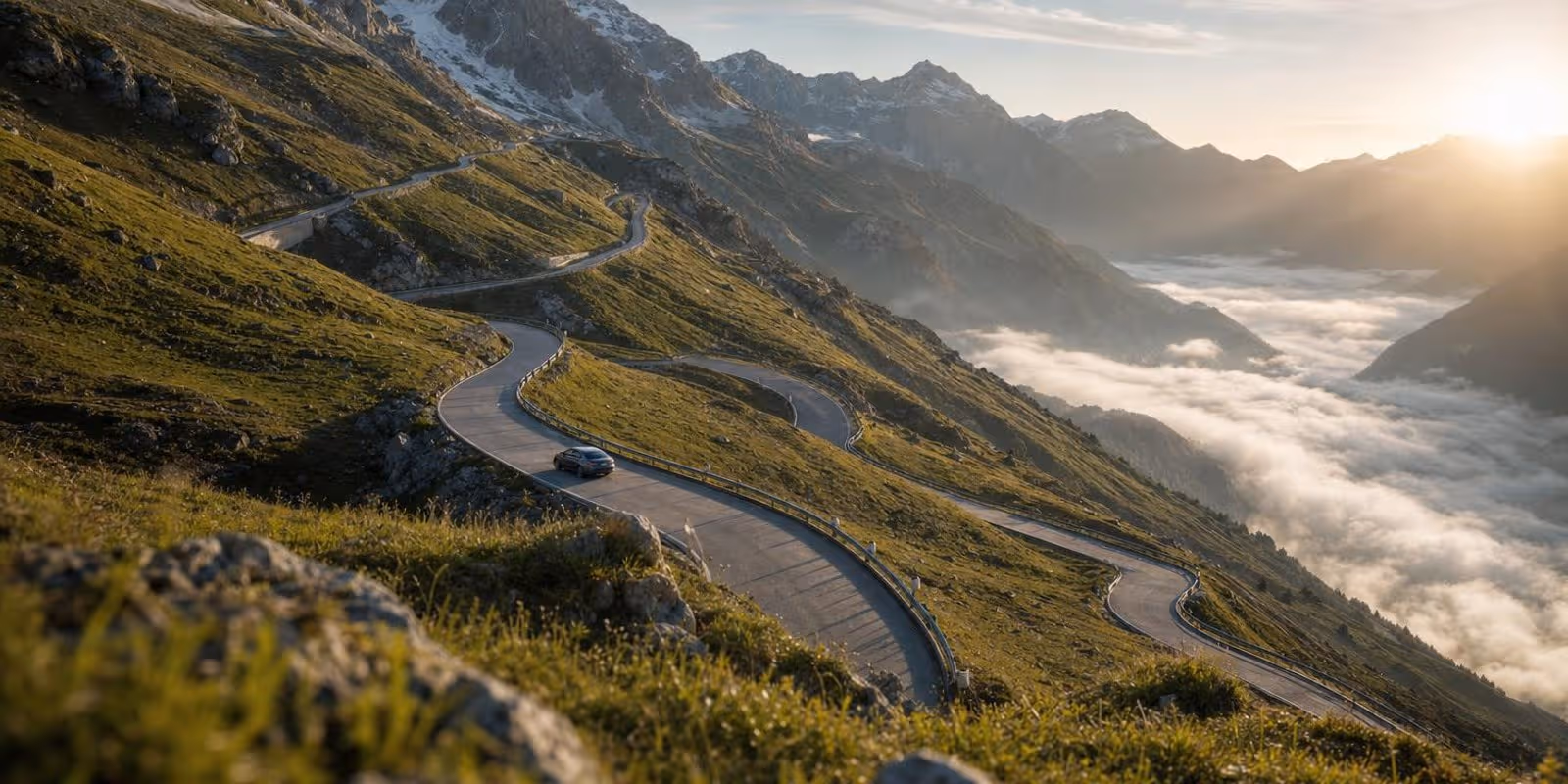 Eine Passstrasse windet sich in engen Serpentinen einen gruenen Alpenhang hinauf, ein einzelnes Auto faehrt bergwaerts.
