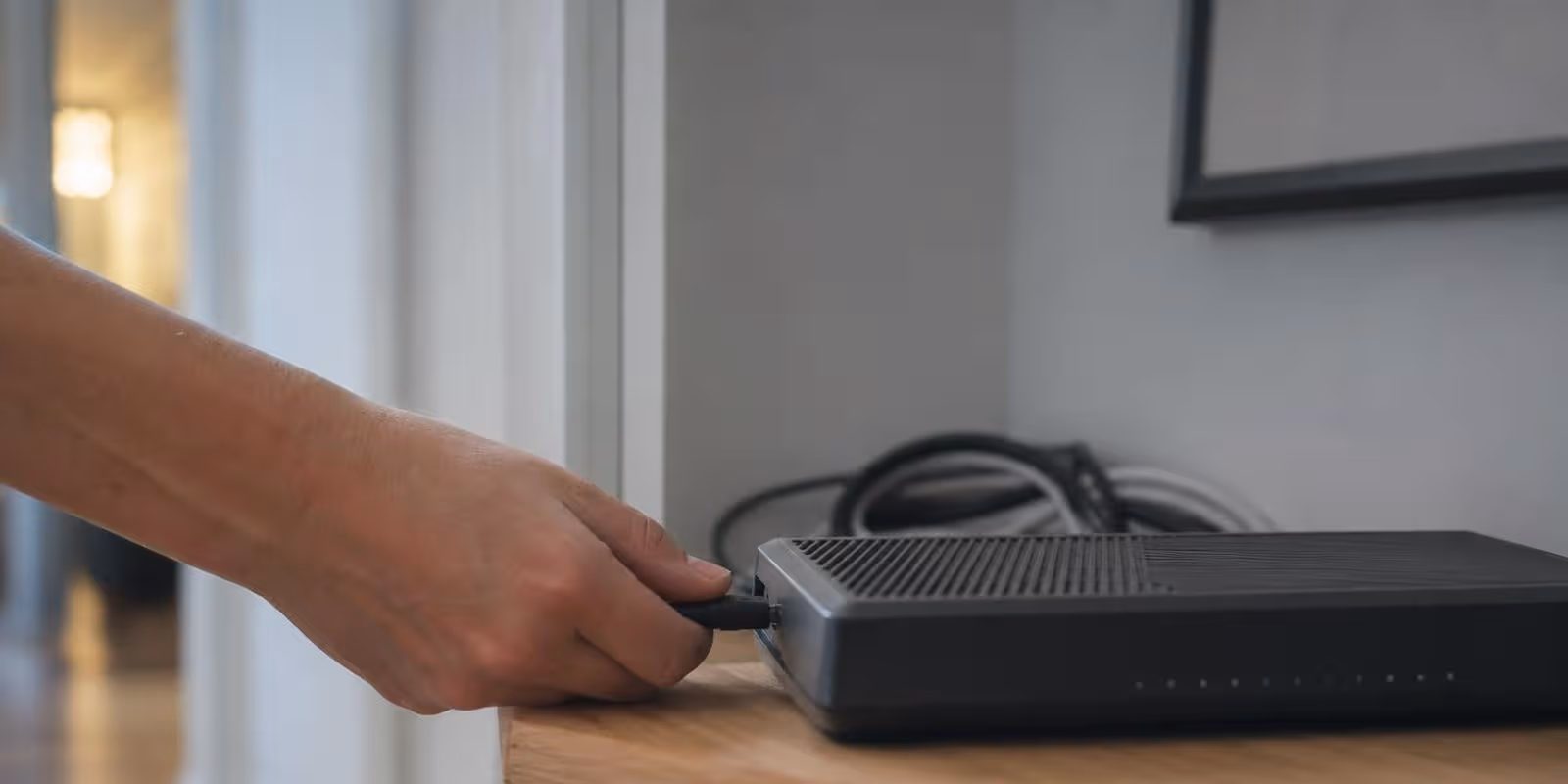Eine Hand zieht den Netzstecker des Routers, dessen Leuchtanzeigen gerade erloeschen.
