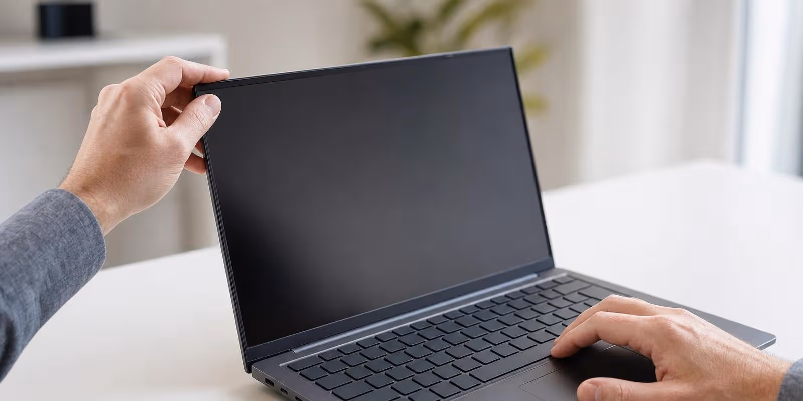 Haende pruefen Scharnier und Tastatur eines gebrauchten Business-Laptops auf einem Schreibtisch.