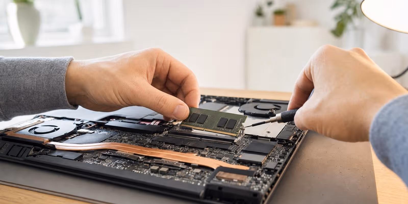 Haende setzen mit einem kleinen Schraubendreher einen RAM-Riegel in einen geoeffneten Laptop ein.
