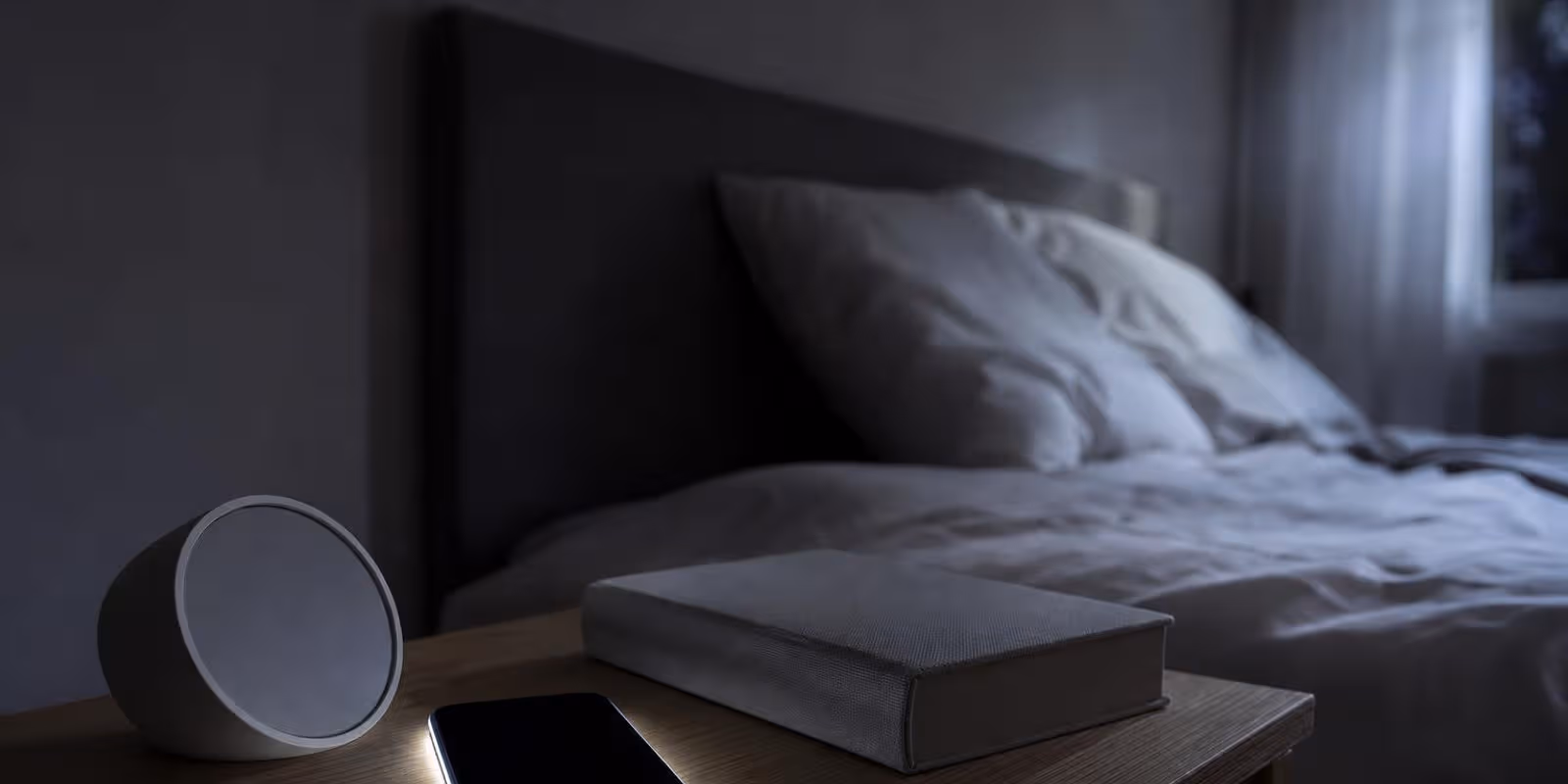 Smartphone laedt nachts am Kabel auf dem Nachttisch neben Wecker und Buch.