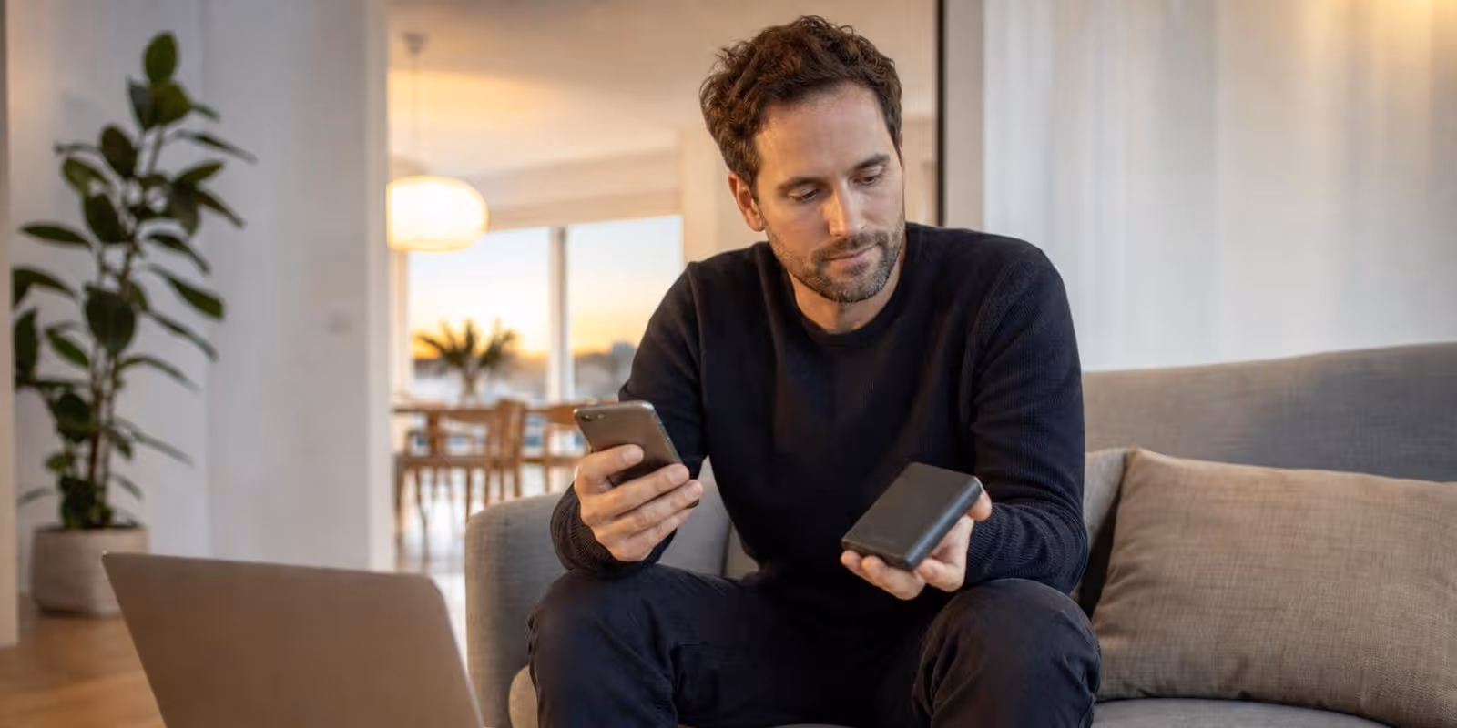Person sitzt mit dem Handy in der einen und einer kleinen externen Festplatte in der anderen Hand.