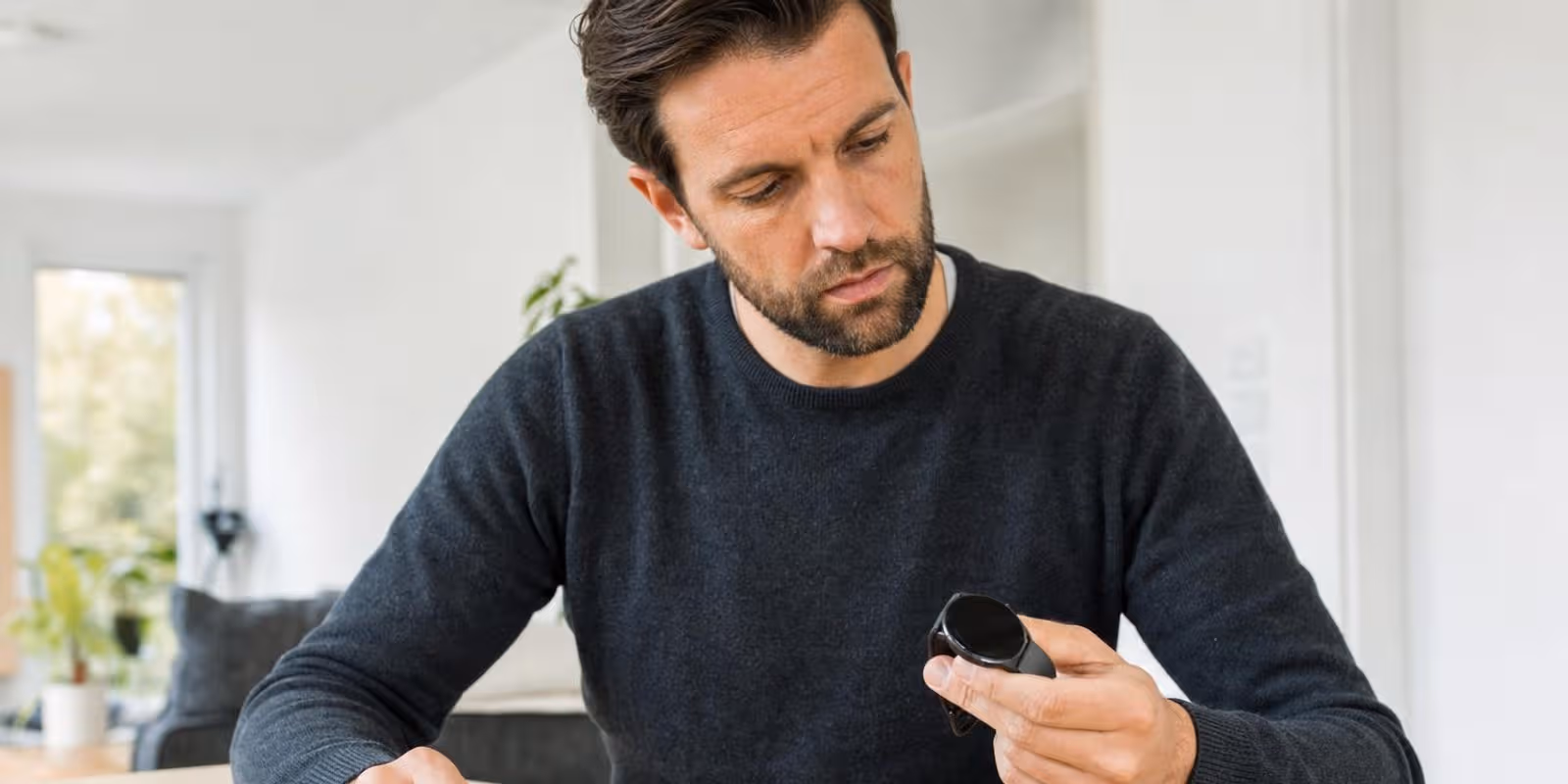 Ein Mann vergleicht am Tisch eine robuste Sportuhr mit Knoepfen und eine schlanke Smartwatch.